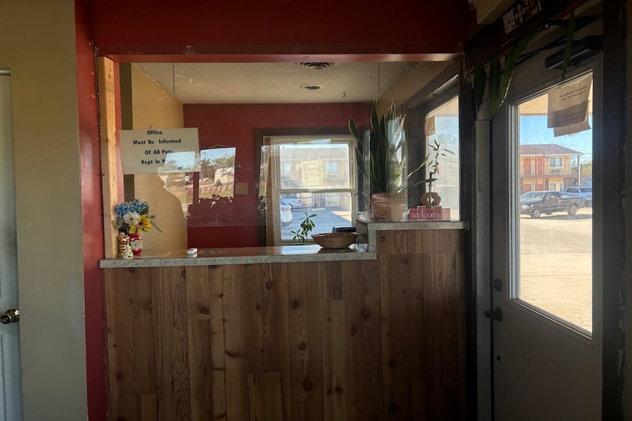Un espace d’accueil avec un comptoir en bois, un panneau indiquant qu’il faut informer le bureau de la présence de tout animal de compagnie, et une vue sur l’extérieur par une fenêtre.