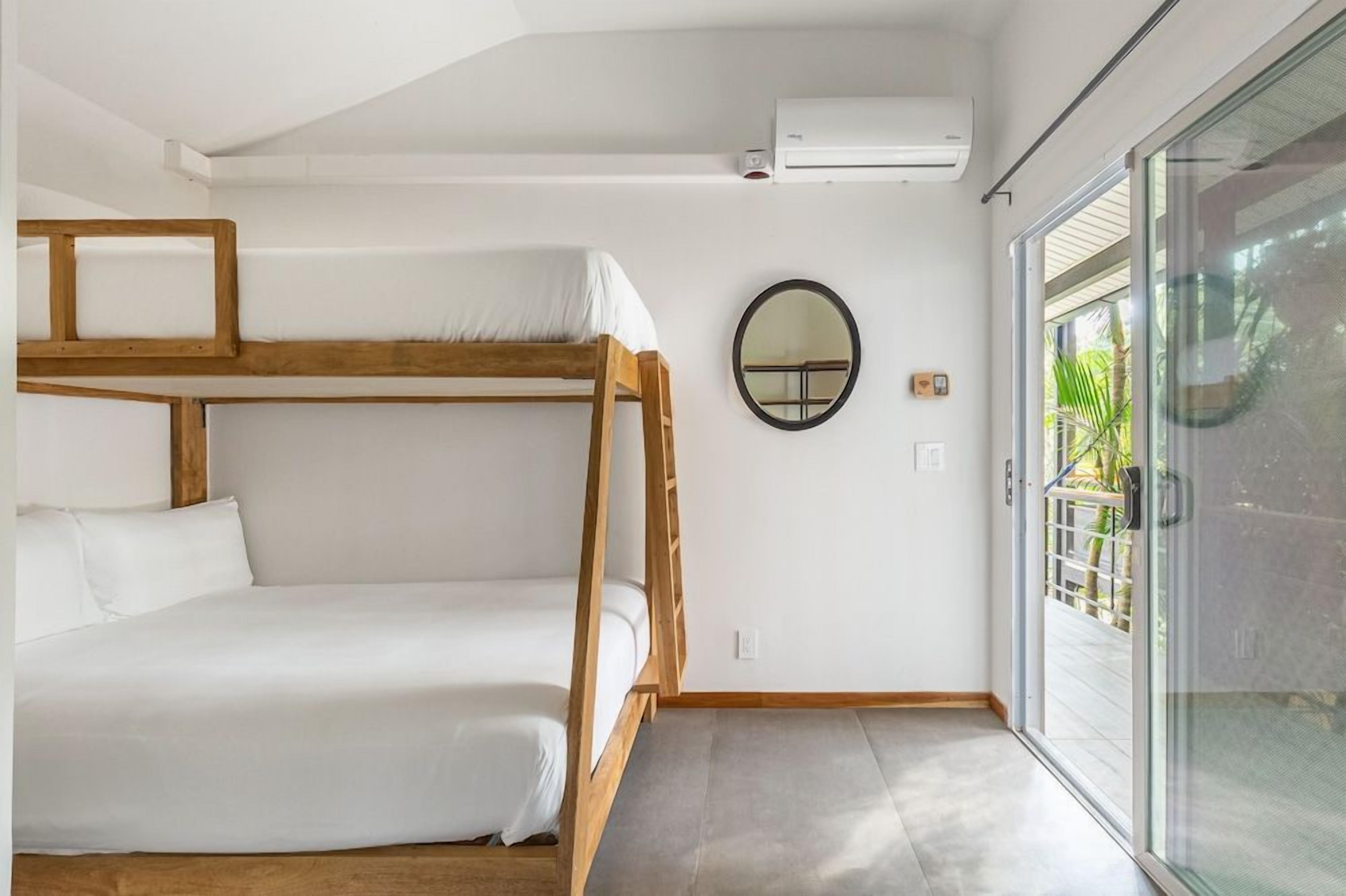 A bunk bed with a wooden frame, a round mirror on the wall, and a sliding glass door leading to an outdoor area.