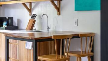 A kitchen with a wooden island, two wooden chairs, a coffee machine, and a teal artwork on the wall.