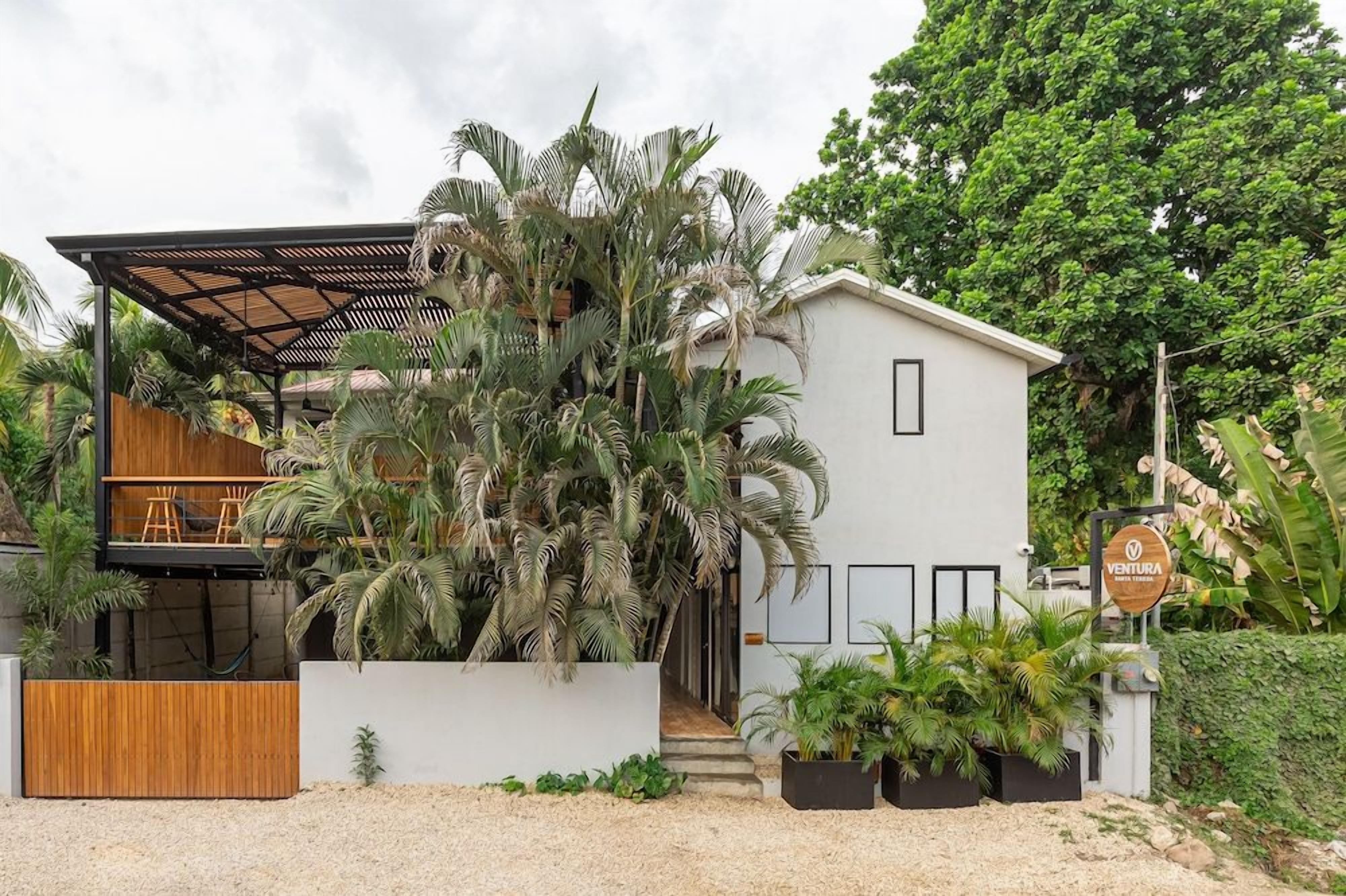 A modern house with a covered outdoor seating area, surrounded by lush tropical plants.