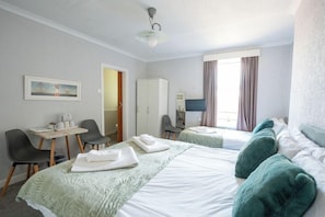 Habitación de hotel con dos camas, un escritorio con una silla, un televisor y un cuadro en la pared.