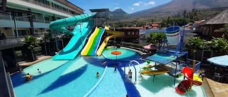 A water park with multiple slides and pools, surrounded by buildings and a mountain in the background.