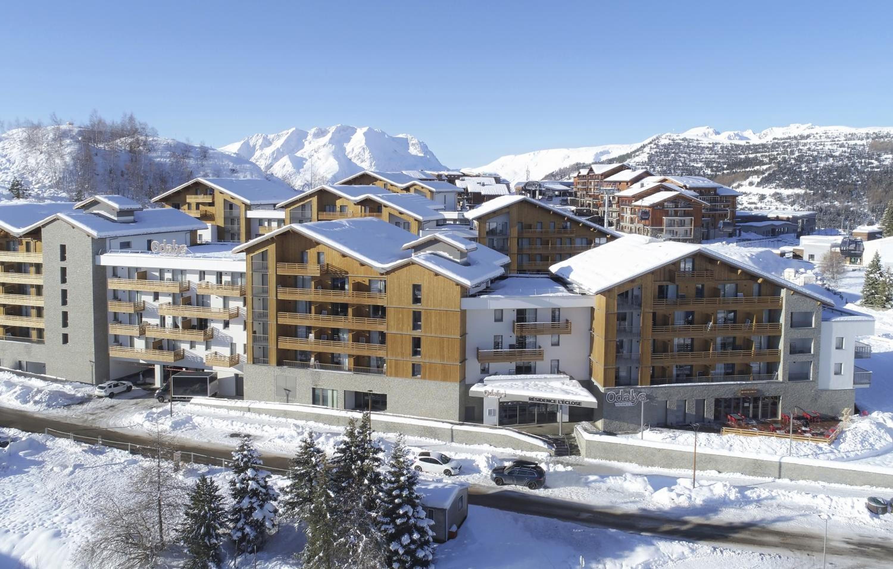 Ein schneebedecktes Resort mit mehreren Gebäuden, darunter ein Hotel mit Balkonen und einer Seilbahn im Hintergrund.