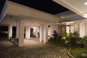 A modern building with a covered entrance, a paved driveway, and a well-maintained garden with various plants. - Hotel GM 253 (Patrang)