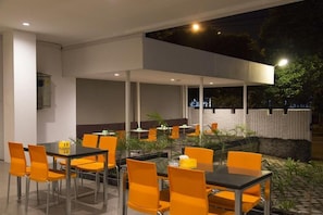 An outdoor dining area with tables and chairs, surrounded by plants and a stone wall. - Hotel GM 253 (Patrang)