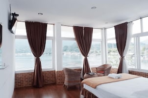 Quarto de hotel com cama, uma cadeira e vista para a água através de grandes janelas.