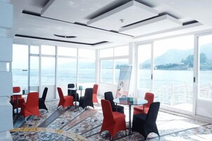 Quarto com janelas amplas, piso estampado e cadeiras vermelhas e pretas ao redor de uma mesa.