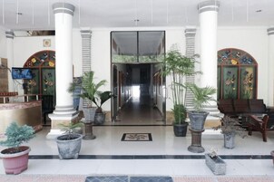 Um saguão de hotel com balcão de recepção, plantas em vasos e área de estar.