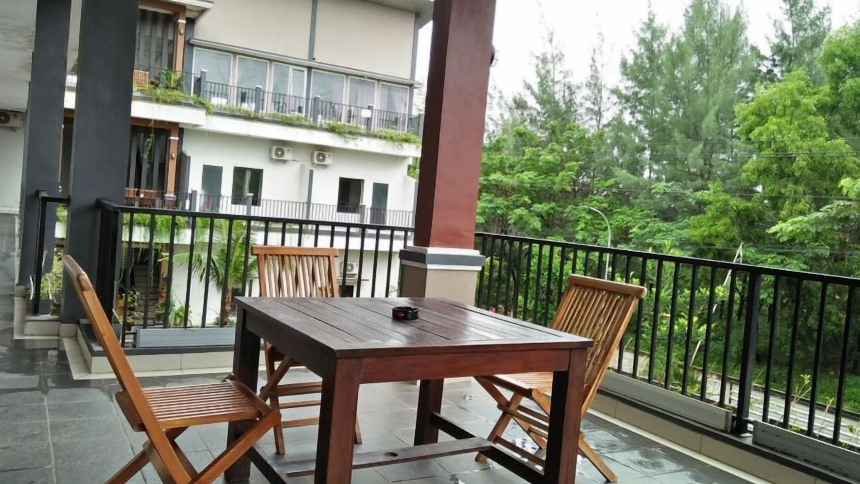 A balcony with a wooden table and chairs, a railing, and a view of a building with balconies and greenery.