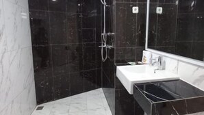 Casa de banho moderna com chuveiro em mármore preto, lavatório branco e um espelho grande.