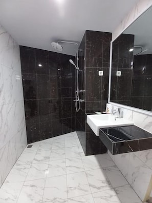 Un baño moderno con ducha de mármol negro, lavamanos blanco y un espejo grande.