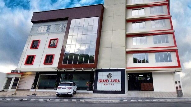Hotel de vários andares com uma placa chamativa, um carro estacionado na frente e um céu claro.