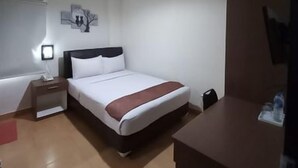 Quarto de hotel com cama, mesa de cabeceira, escrivaninha e uma secretária com cadeira.