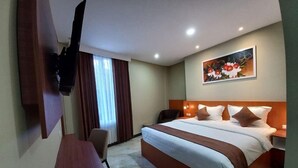 Quarto de hotel com uma cama, uma escrivaninha, uma cadeira, uma TV fixada na parede e um quadro na parede.