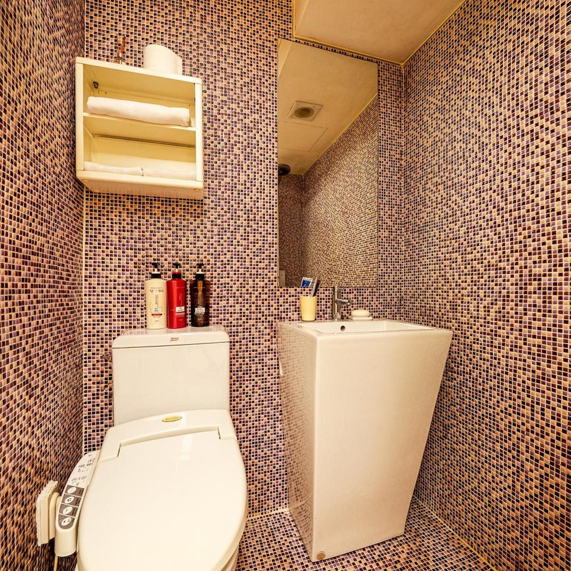 A bathroom with a toilet, a sink, and a mirror. There are toiletries on the sink counter.