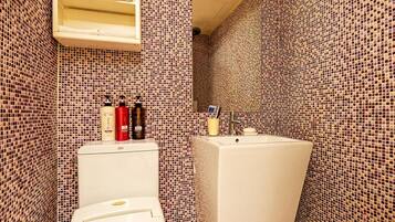 A bathroom with a toilet, a sink, and a mirror. There are toiletries on the sink counter.