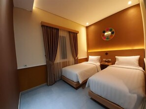 A hotel room with two beds, a nightstand, a wall-mounted decorative item, and a window with curtains. - Americano Syariah Hotel Jogja (Sewon)