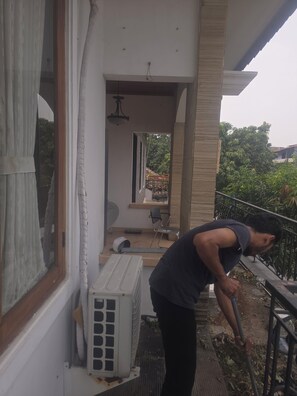 A balcony with a person leaning on the railing, a window with curtains, and an air conditioning unit.