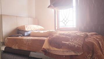 A single bed with a mattress, pillows, and a blanket in a room with a window and curtains.