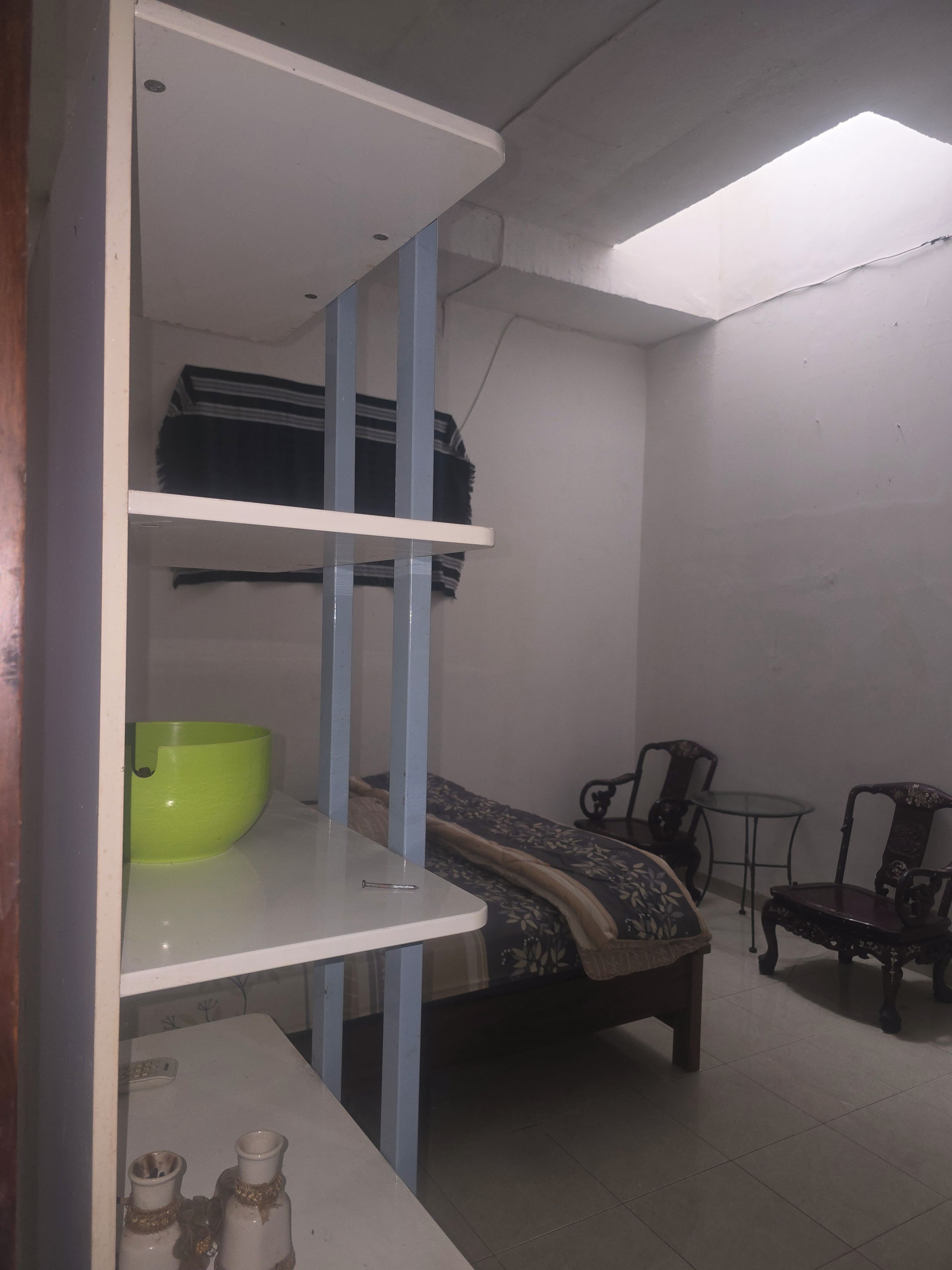 Una habitación con una cama, una mesita, una silla y un estante con un cuenco.