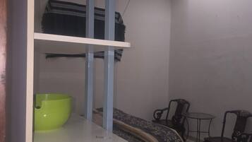 A room with a bed, a small table, a chair, and a shelf with a bowl.