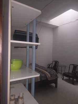 A room with a bed, a small table, a chair, and a shelf with a bowl.