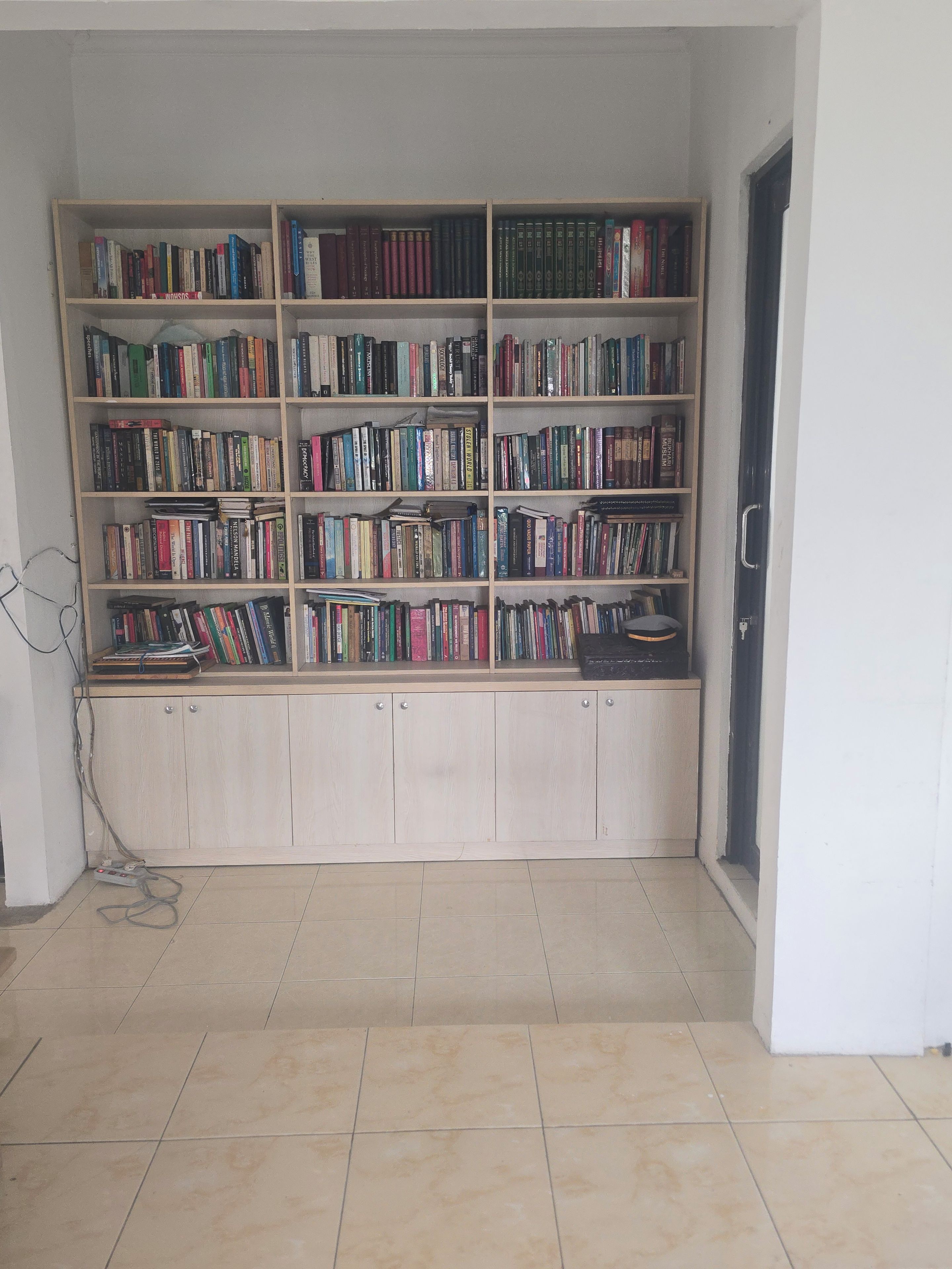 A room with a large bookshelf filled with books, a wooden cabinet, and a tiled floor.