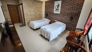 Habitación de hotel con dos camas, un escritorio, una silla y una pared de ladrillo con un cuadro.
