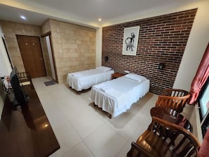 Ein Hotelzimmer mit zwei Betten, einem Schreibtisch, einem Stuhl und einer Ziegelwand mit einem Bild.
