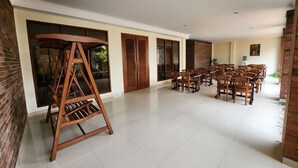 Un espacio interior amplio con un gran conjunto de columpios de madera, varias sillas de madera y suelo de baldosas.