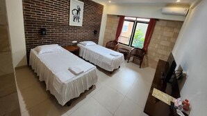 Habitación de hotel con dos camas, una pequeña zona de estar, televisor y pared de ladrillo.