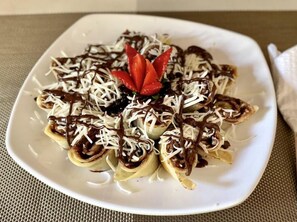 Une assiette blanche contenant un plat, peut-être un dessert, recouvert de chocolat et de fromage râpé, et décoré d’une tranche de fruit rouge.