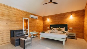 A wooden-paneled room with a bed, a mirror, a small table, a sofa, and a ceiling fan. - Stone Wood Jungle Resort - Dandeli (Joida)