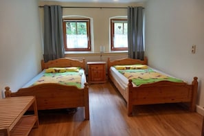 A room with two wooden beds, a small wooden table, and a window with curtains. - Holiday apartment with 2 bedrooms (Geiselwind)