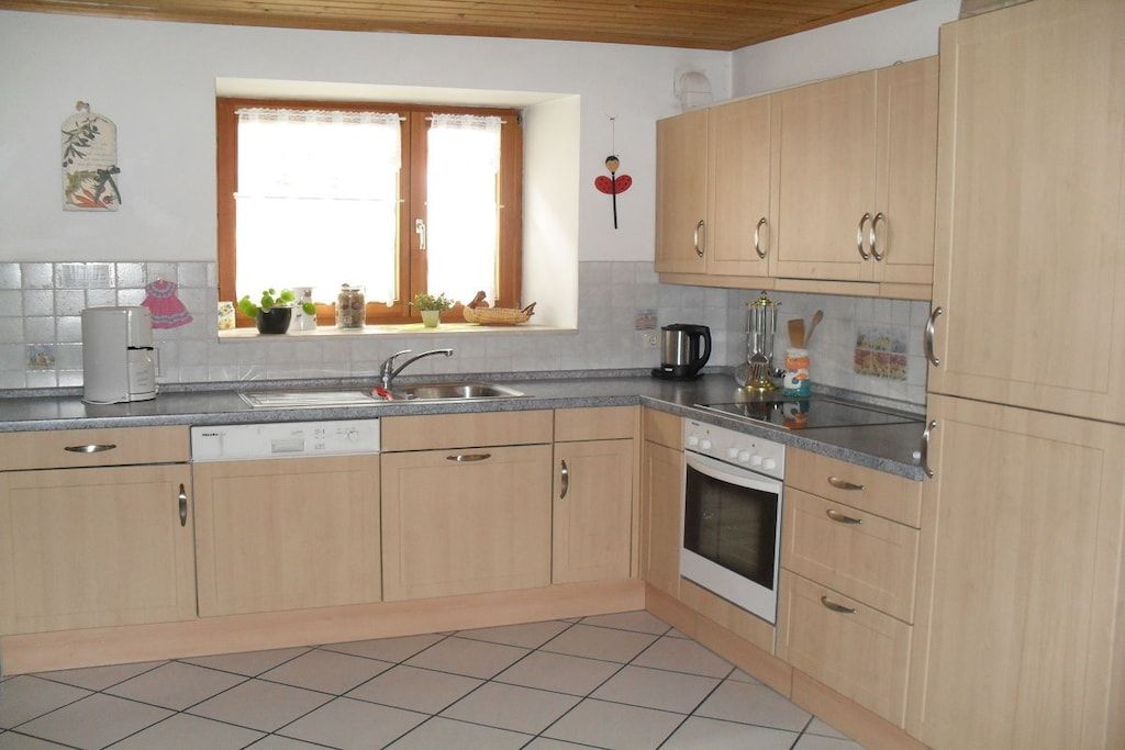 Una cocina con armarios de madera, lavavajillas, estufa y ventana con plantas.