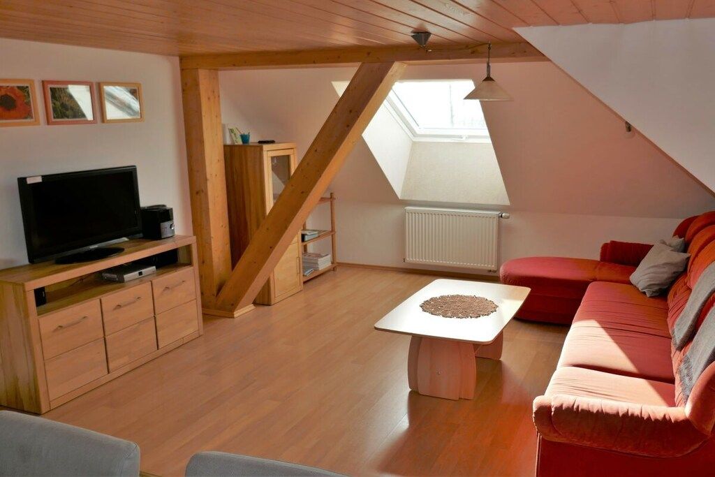 A cozy loft-style living room with a wooden ceiling, a flat-screen TV, a red sofa, and a small table with a decorative item.