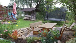 Un jardín con un banco de madera, una mesa de picnic, un trampolín y una pequeña estructura de madera con un tobogán.