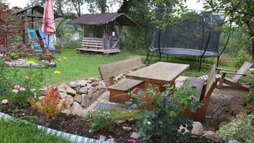 A garden with a wooden bench, a picnic table, a trampoline, and a small wooden structure with a slide.
