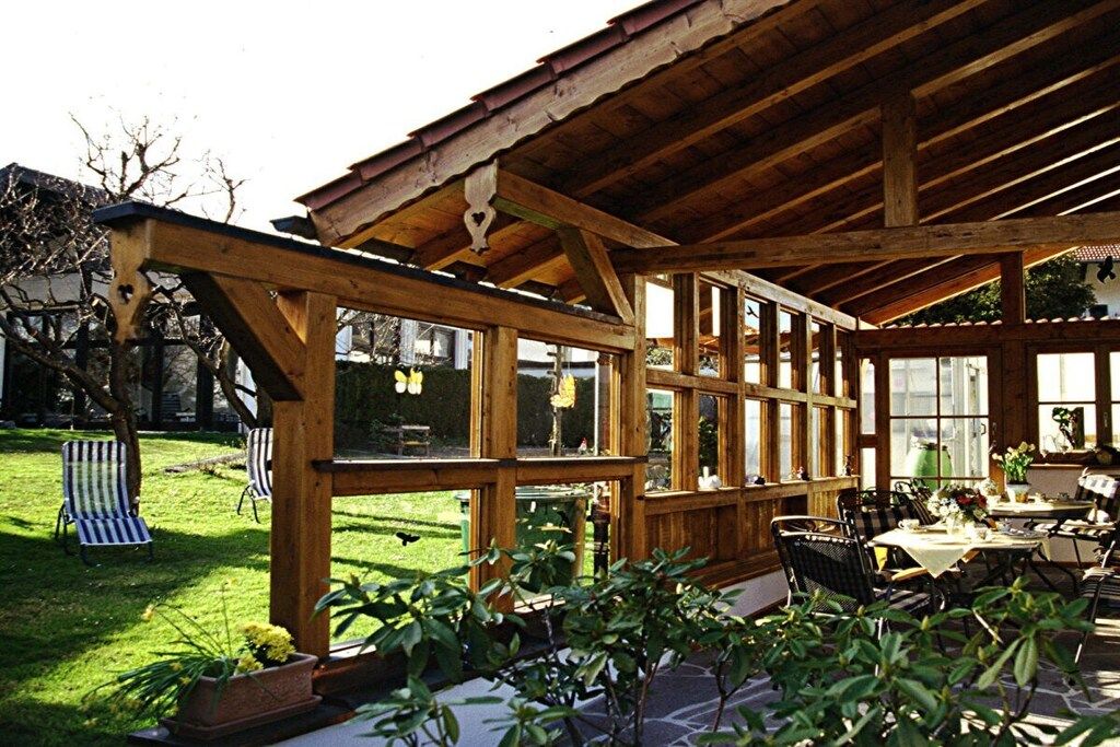 Ein überdachter Außenbereich mit Holzbalken, einem Esstisch, Stühlen und Blick auf einen Garten.