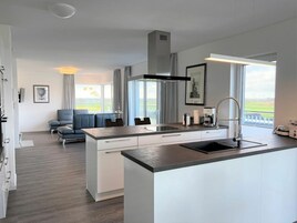 A modern kitchen with a central island, a dining area with a sofa, and large windows offering a view of the outdoors.