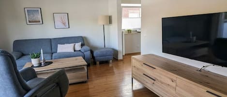 A modern living room with a grey sofa, a wooden coffee table, a grey armchair, and a TV on a wooden stand.