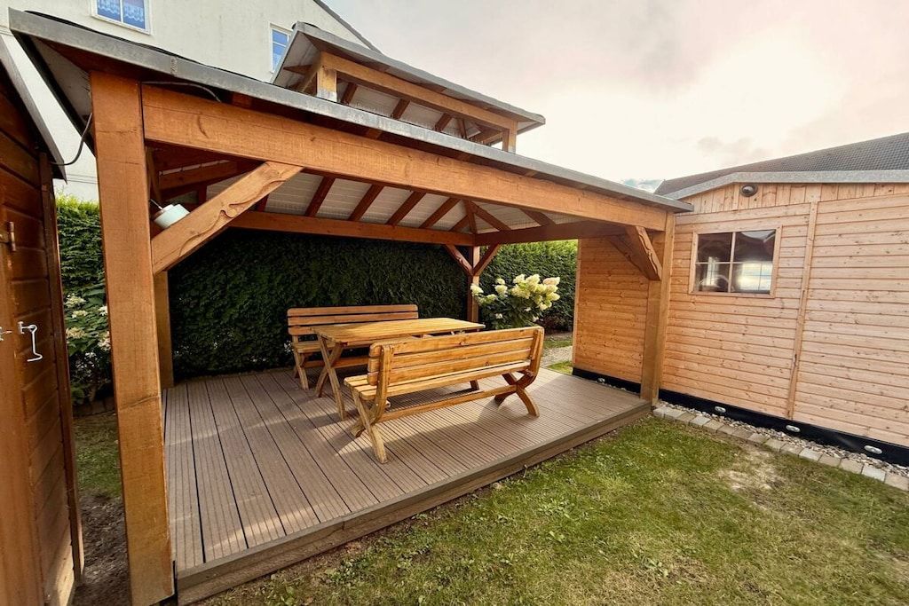 Una terraza de madera con un pérgola, una mesa y bancos.