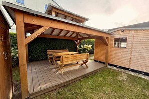 Un terrazzo in legno con una pergola, un tavolo e panche.