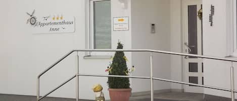 Une entrée d’immeuble avec un escalier, une petite plante en pot et une figurine décorative.