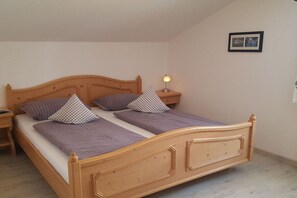Un lit simple avec une tête de lit en bois, deux oreillers, une lampe de chevet et un tableau encadré accroché au mur.