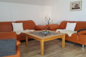 A modern living room with two orange sofas, a glass-top coffee table, and a wall-mounted candelabra. - Holiday apartment with 2 bedrooms (Bad Hindelang)
