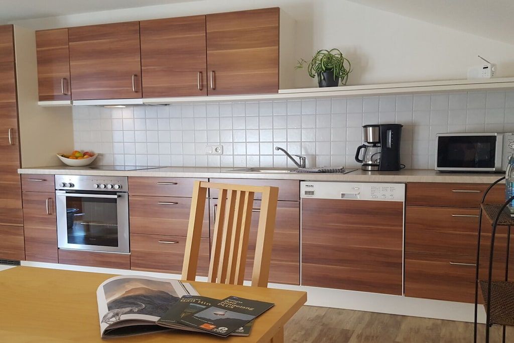 A modern kitchen with wooden cabinets, a built-in oven, a coffee maker, and a dishwasher.