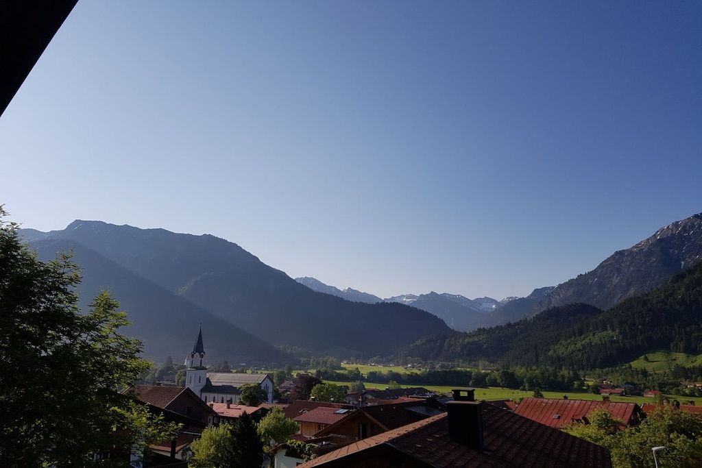 Un village de montagne aux bâtiments traditionnels, avec une église et une vallée parsemée de champs.
