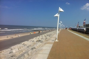 A coastal walkway with a stone barrier, flags, and a clear view of the ocean. - Kaiserhof 002 Reinke am Strand (Norderney)