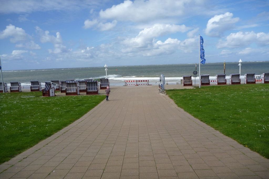 Uma passarela pavimentada que leva a uma praia com cadeiras de praia e uma bandeira.